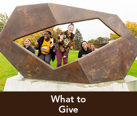 Rollover image of students posing around a sculpture. Link to What to Give.
